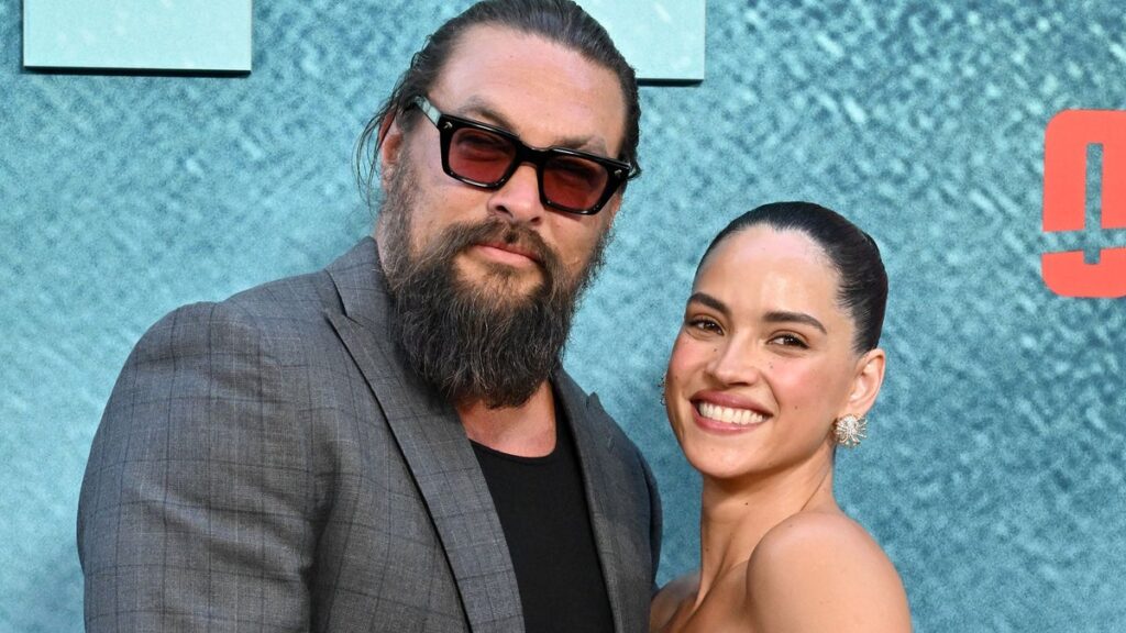 Adria Arjona and Jason Momoa share a sweet kiss on the ‘Onslaught’ red carpet